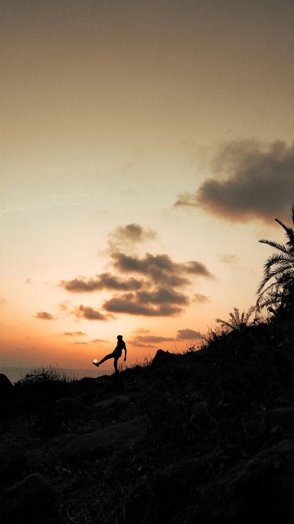 Silhouette of a lone person kicking high in front of a colorful sunset sky on a hill.