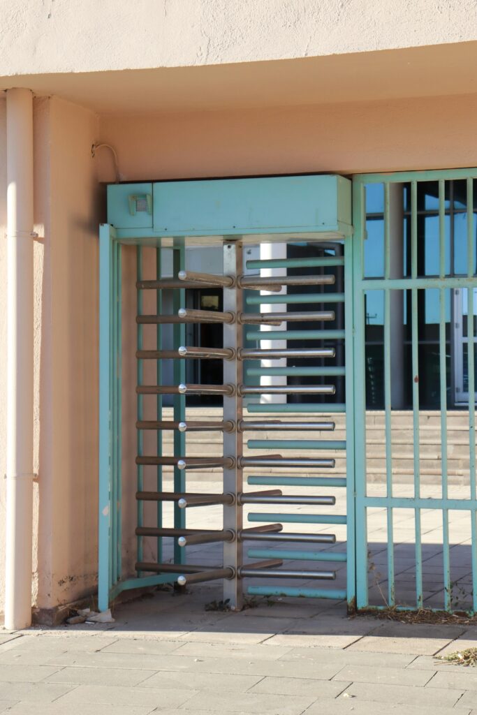 Rustic turquoise turnstile and gate entrance to a building, bathed in natural light.