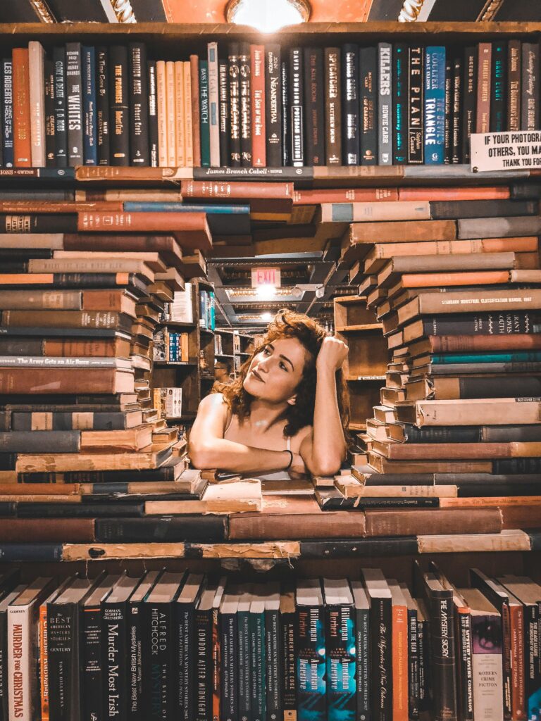 A woman framed by books poses inside a library with a charming smile.