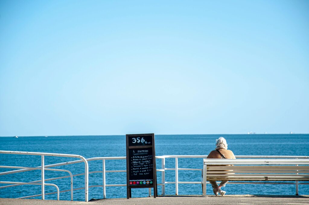 Elderly woman enjoying a sunny day on a bench by the sea in La Baule, France.