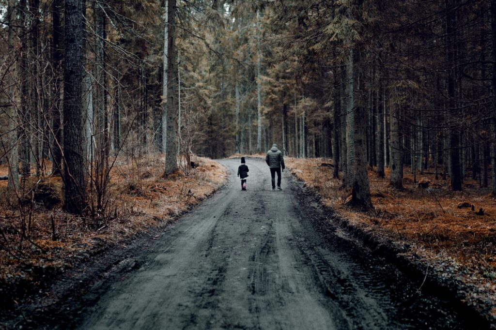Father and child walking on a forest trail during fall, surrounded by trees and nature.