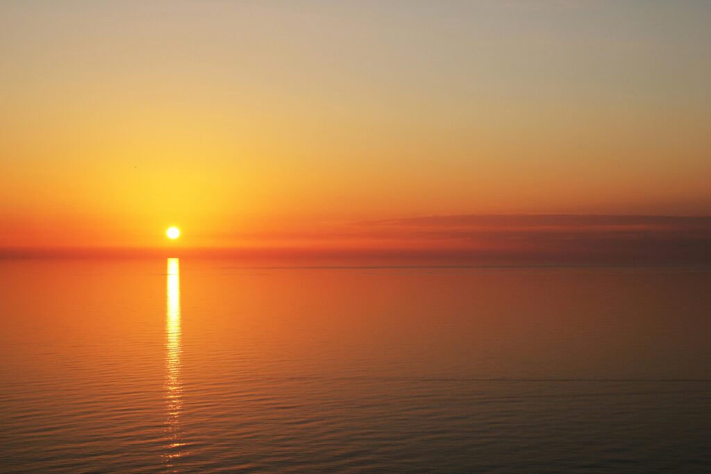 A tranquil sunset over calm ocean waters with golden reflections in the sky and sea.