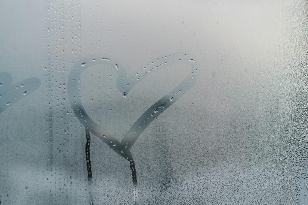 A heart shape drawn on a foggy window with water droplets streaming down for a romantic touch.