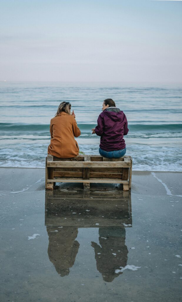 Two women sitting on a pallet by the Odesa shoreline, enjoying the serene sea view.