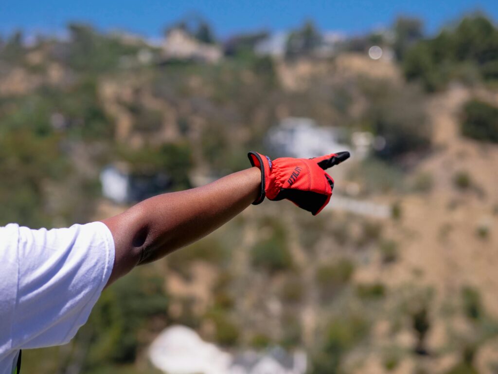 Close-up of a gloved hand pointing outdoors with a blurred natural background.