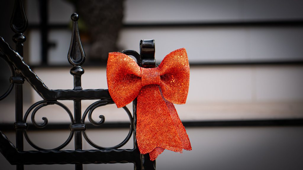Close-up of an orange bow decorating a black wrought iron fence, evoking festive and elegant vibes.