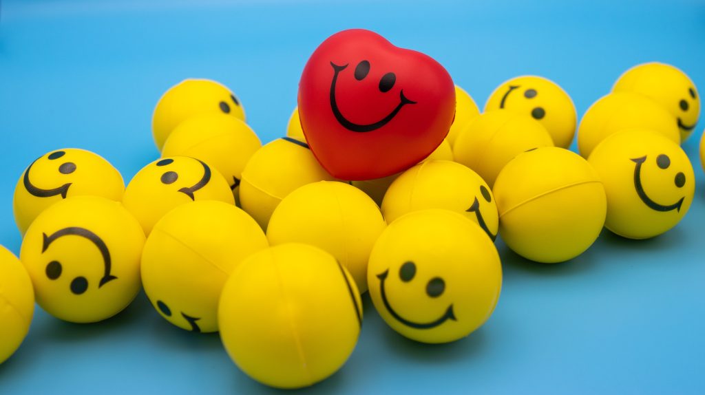 Bright yellow smiley face balls with a standout red heart-shaped ball on a blue surface.