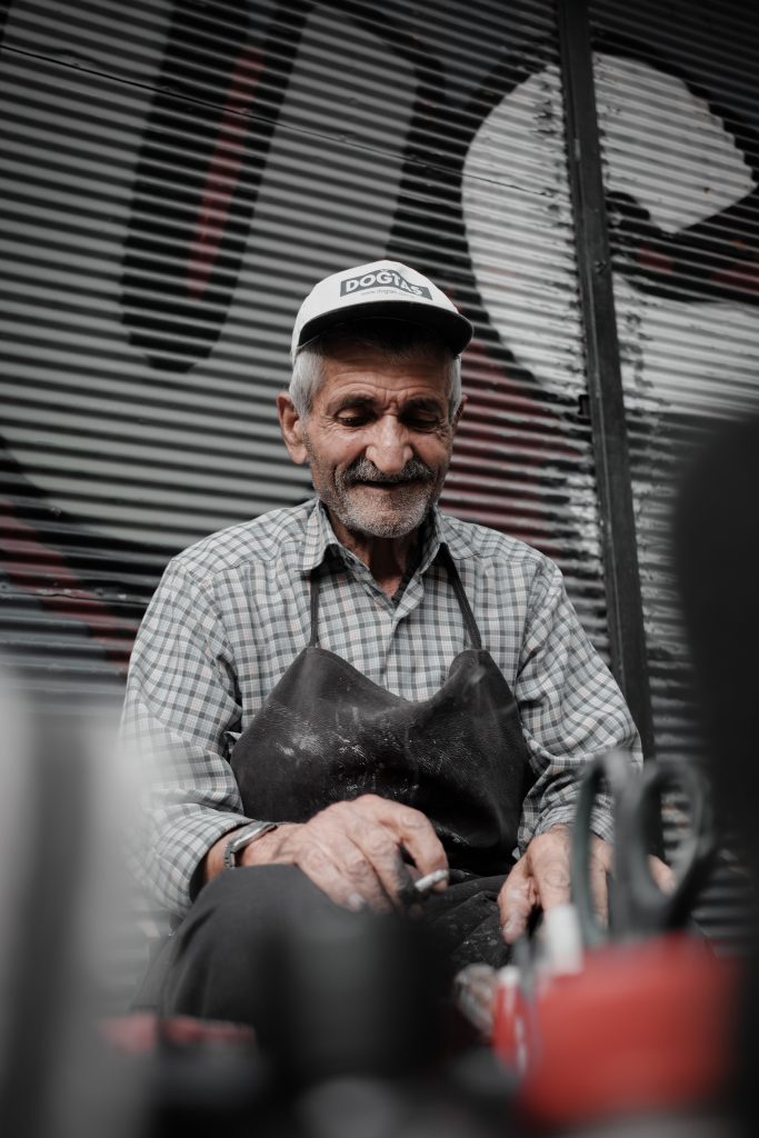 Elderly man wearing a cap working diligently outdoors, urban setting.